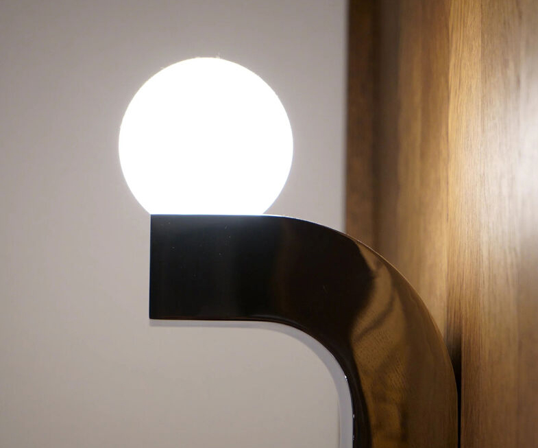 Pallia Wall Lighting - Practical and Decorative Detail 3 Pallia wall lamp with curved wooden arm and glowing spherical bulb mounted on a wooden panel.