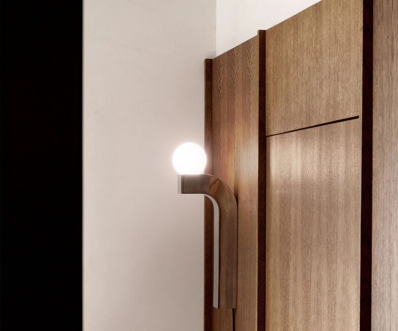 Pallia Wall Lighting - Practical and Decorative Detail 4 Pallia wall lamp with curved wooden arm and glowing spherical bulb mounted on a wooden panel.