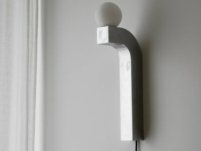 Pallia wall lamp with curved wooden arm and glowing spherical bulb mounted on a wooden panel.