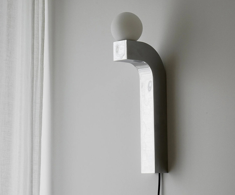 Pallia Wall Lighting - Practical and Decorative Detail 1 Pallia wall lamp with curved wooden arm and glowing spherical bulb mounted on a wooden panel.